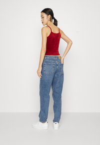 Top de malha vermelho em veludo com alças finas, combinado com calças de ganga azuis de corte solto. Ténis brancos completam o visual. Design simples e casual.