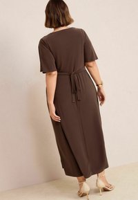 Braunes, kurzärmeliges Maxikleid mit Bindegürtel und seitlichen Schlitzen. Glatter Stoff mit lässiger Passform, kombiniert mit hellen, hochhackigen Schuhen.