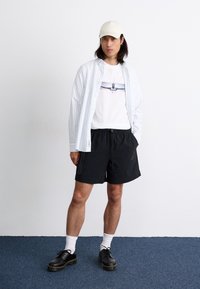 White striped long-sleeve shirt, graphic t-shirt, black shorts, white socks, black shoes with yellow sole, beige cap. Minimalist design.