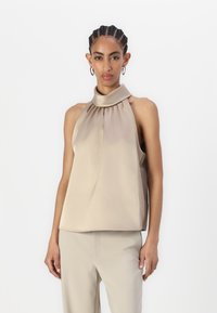 Top halter beige con scollo plissettato, realizzato in tessuto morbido, caratterizzato da una vestibilità morbida e senza chiusure visibili o motivi.