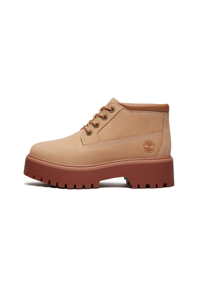 Stivaletti beige in pelle con rifiniture marroni, punta rotonda e suola in gomma spessa, con lacci e un logo ad albero sul lato.