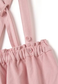 Prenda sin mangas de color rosa con una tela texturizada, que cuenta con tirantes ajustables, cintura fruncida y dos botones a juego.
