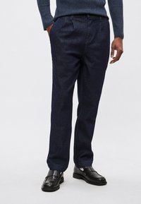 Tmavomodré nohavice z denimu s voľným strihom, skladaným predným dielom a bočnými vreckami. Kombinované s čiernymi koženými mokasínami.