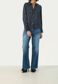 Langslalig navy shirt met luipaardprint, met knopen aan de voorkant, gecombineerd met blauwe hoge taille flared jeans en zwarte hakken met ruffles.