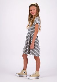 Gestreiftes Kleid in Marineblau und Weiß, kurze Ärmel, ausgestellter Rock, kombiniert mit beigen High-Top-Sneakers. Glattes Material, lässiges Design.