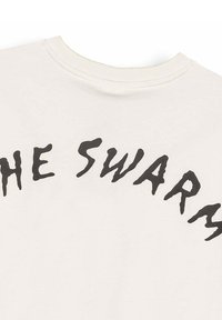 T-shirt w kolorze ecru z okrągłym dekoltem, z nadrukowanym czarnym zniekształconym tekstem na piersiach, czytającym "ROJ".