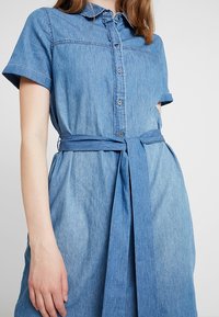 Helles blaues Denim-Kleid mit kurzen Ärmeln, Knopfleiste, Kragen und tailliertem Gurt. Verfügt über eine lockere Passform und eine glatte Textur.
