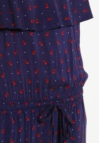 Marinblå klänning med röd ankarmönster och vita prickar. Har rynkad halsringning, påsydd midja och dragsko. Mjuk tygtextur.