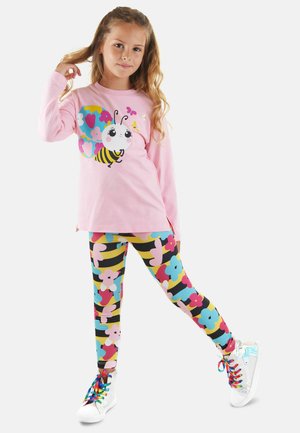 Un haut rose à manches longues avec un graphique de dessin animé d'abeille, associé à un legging floral coloré. Des baskets blanches avec des lacets arc-en-ciel complètent la tenue.