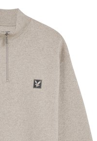 Pullover grigio chiaro con zip a un quarto, realizzato in morbido tessuto. Presenta un piccolo emblema scuro con un design di un uccello nella zona sinistra del petto.