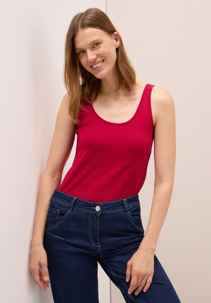 Red sleeveless top made of stretch fabric, paired with dark blue denim jeans featuring a button closure and front pockets.