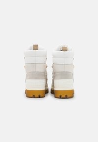 Sneaker alte bianche e beige con superficie testurizzate, colletto imbottito, dettagli in hardware dorato e suola in gomma con battistrada marrone a contrasto.