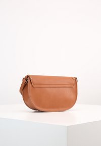 Borsa a tracolla in pelle marrone con forma arrotondata, chiusura a pattina e un accento laterale testurizzato. Presenta una tracolla regolabile e sottile.