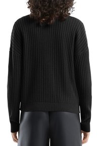 Czarny sweter dziany o fakturze przypominającej wzór waflowy, z luźnym krojem oraz ściągaczami przy mankietach i dole. Projekt uwzględnia opuszczone ramiona dla większego komfortu.