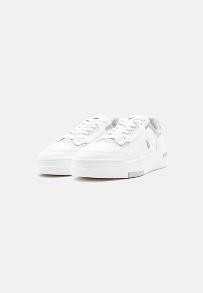 Paire de baskets basses blanches à lacets, avec des accents gris et un petit logo brodé sur le côté, présentées sur un fond uni.