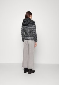 Svart huva jacka med en quiltad design och ett upprepande logomönster. Matcherade med vida grå byxor och svarta skor.