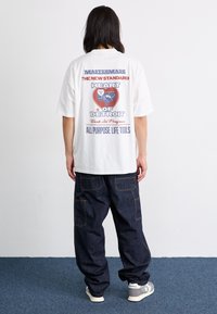 White t-shirt featuring a colorful graphic print on the back, paired with dark denim pants and gray sneakers with white accents.