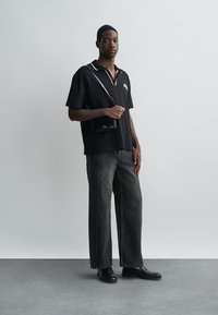 Černé polo tričko s krátkým rukávem a bílým detailem na límečku, spárované s šedými širokým střiženými džíny. Doplňky zahrnují malou černou crossbody tašku a černé boty.