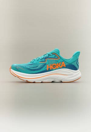 Teal en oranje HOKA hardloopschoen met witte dikke zool, mesh bovenwerk en oranje branding aan de zijkant, gezien vanaf de buitenkant.