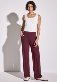 Un débardeur blanc et un pantalon large bordeaux en tissu doux. Le pantalon dispose de poches latérales et d'une taille lisse. Les baskets sont beiges avec des accents blancs.