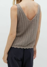 Top in maglia di un marrone chiaro con scollatura a V profonda sul retro, caratterizzato da un design testurizzato e un orlo ondulato. Il materiale appare traspirante e a trama aperta.