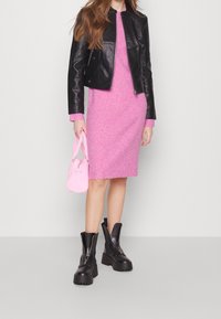 Svart läderjacka, rosa ribbad stickad klänning, rosa handväska och klumpiga svarta plattformskängor. Släta och texturerade ytor, åtsittande silhuett.