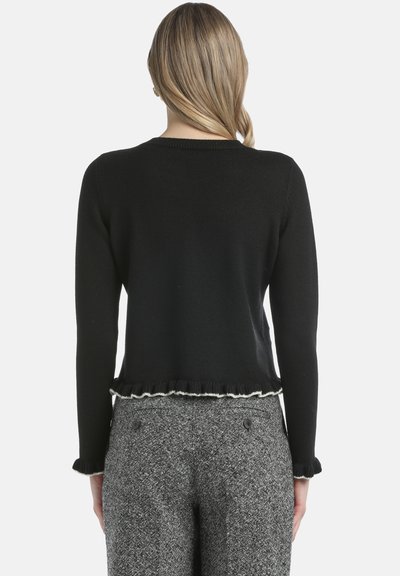 Melnā īsā džemperis ar garām piedurknēm, ribota adījuma tekstūra un ruffles apakšmalā. Kombinēts ar pelēkām houndstooth raksta biksēm.