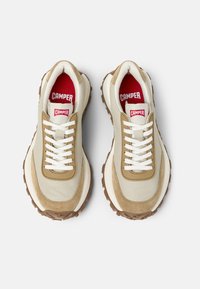 Beiget ja vaaleanruskeat tennarit, joissa on nahka- ja mokkapäällinen, valkoiset kengännauhat, punainen sisäpohja ja kuvioitu ruskea ulkopohja.