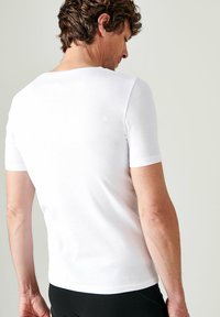 T-shirt bianco a maniche corte realizzato in cotone, dalla vestibilità aderente, texture liscia, scollatura rotonda, cuciture visibili sulle maniche e sull'orlo.