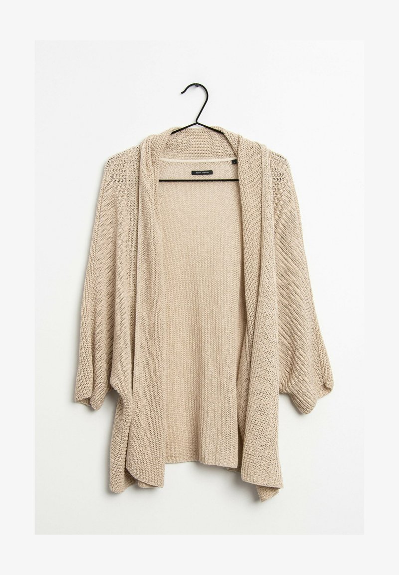 Beige, öppen cardigan med lös passform, långa ärmar och en texturerad stickad mönster. Hänger från en svart krok.