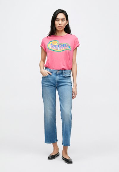 Ruži�časta kratka majica s višebojnim grafičkim uzorkom; uparena s trapericama ravnih nogavica u svijetloj nijansi; crne ravne cipele; minimalistička pozadina.