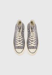 High-top sneakers featuring a grey and black snake print design, white laces, rubber toe cap, and cream-colored sole.