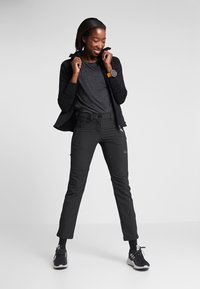 Black zip-up jacket over a dark gray T-shirt, paired with black pants featuring pockets, worn with black athletic shoes.