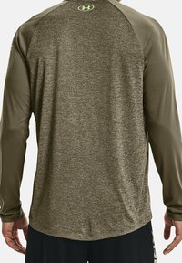 Langärmeliges Sportshirt mit strukturiertem olivgrünem Körper und olivgrünen Ärmeln. Verfügt über ein kleines Logo auf dem oberen Rücken in Neon-Grün.