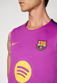 Férfi ujjatlan lila FC Barcelona mezben, sárga Nike logóval és nagy sárga Spotify logóval a mellkasán, látható tetoválással a karján.