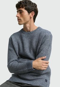 Grauer, gestrickter Pullover mit strukturiertem Muster, Rundhalsausschnitt und gerippten Bündchen. Verfügt über ein kleines Logotäfelchen an der unteren Seite.