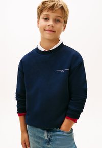 Sweatshirt blu navy con polsini a coste, caratterizzato da un logo bianco sul petto. Combinato con jeans blu chiaro, che mostrano un fit casual.