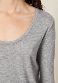 Približen posnetek zgornjega dela prsnega koša in rame osebe, ki nosi dolgotrajno sivo majico z okroglim izrezom na vratu.