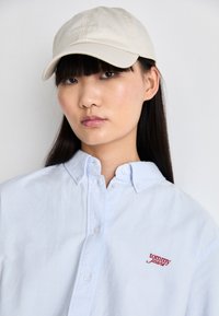 Beige caps med "TOMMY JEANS" logo. Lys blå skjorte med knapper og rød "tommy" brodering. Glatt stoff, klassisk kragedesign.