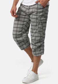 Grå ternede cargo shorts med en afslappet pasform, der har sidelommer og knælang skæring, fremstillet af letvægtsstof. Hvide sneakers synlige.