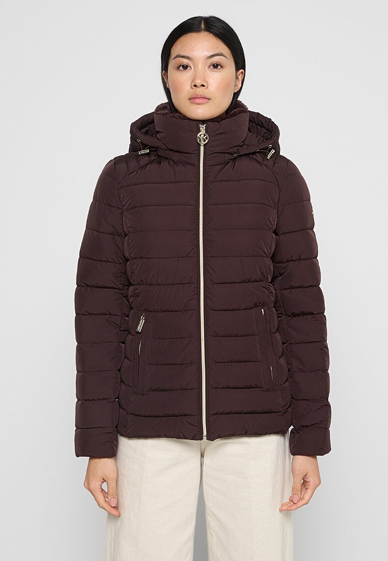 Veste matelassée bordeaux avec capuche, fermeture éclair et poches latérales ; présente un motif matelassé horizontal et des accessoires en ton doré.