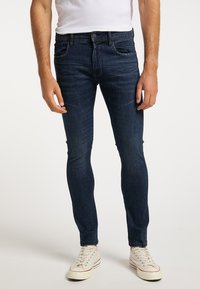 Tummansiniset slim-fit farkut, joissa on keskikorkea vyötärö, etu- ja takataskut, hillitty haalistuminen ja vähäiset ompelusarjat. Yhdistetty valkoisiin lenkkitossuihin.