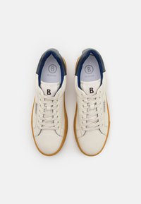 Hvit lær sneakers med brune gummisåler, blå og grå detaljer, rund tå og snøring. Har preget logo på tungen.