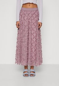 Lång, lätt kjol i ljusrosa med texturerade blommor, med ett elastiskt midjeband. Bärs med blå sandaler med tvinnade remmar.