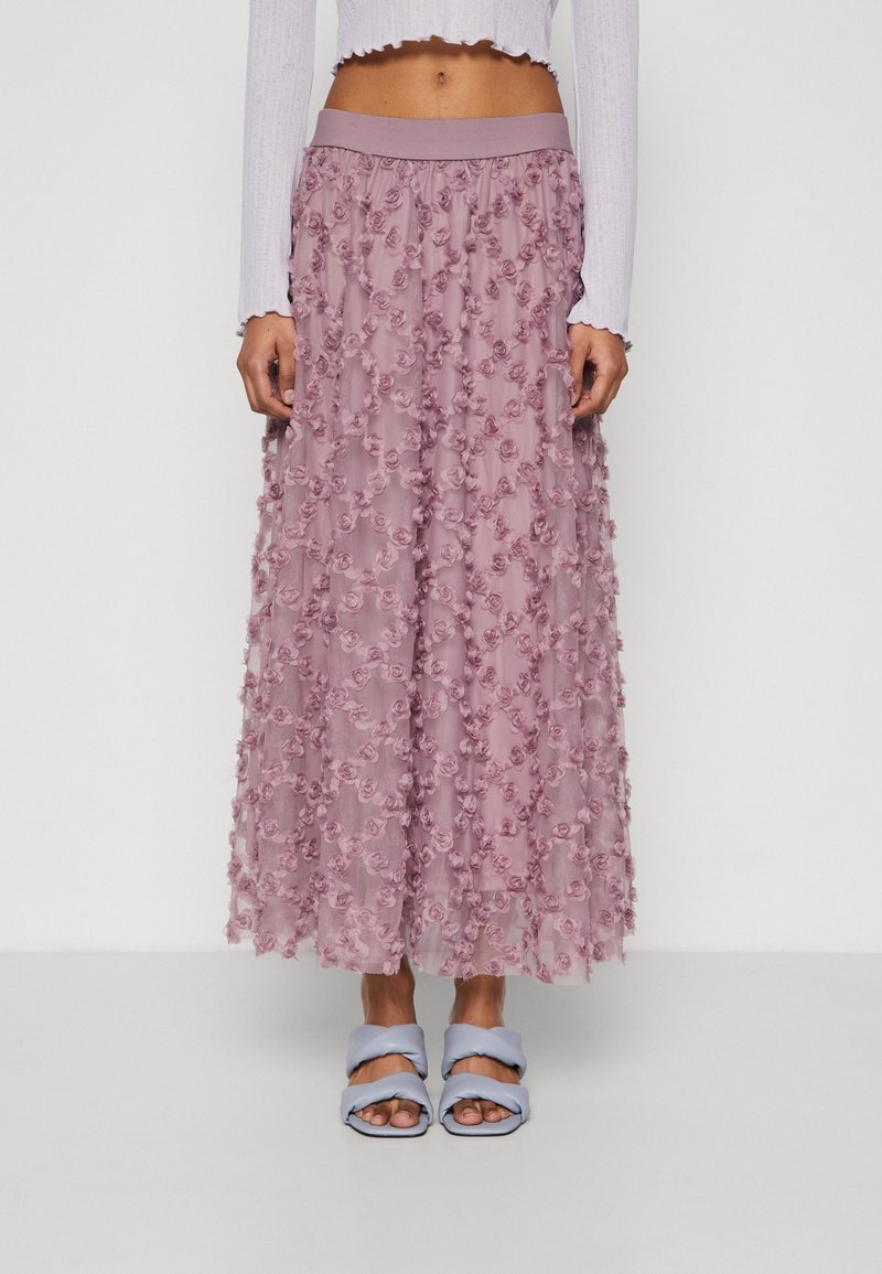 Lång, lätt kjol i ljusrosa med texturerade blommor, med ett elastiskt midjeband. Bärs med blå sandaler med tvinnade remmar.