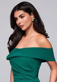 Grön off-shoulder-klänning i mjukt tyg med draperade detaljer och en figurnära överdel. Anmärkningsvärda gyllene blommörhängen kompletterar looken.