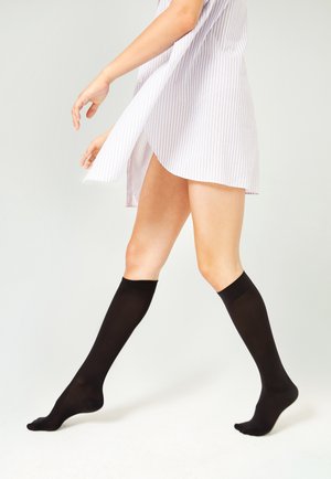 Schwarze kniehohe Socken aus einem glatten, dehnbaren Material. Das Design ist schlank mit einer einfarbigen Optik und einem angenehmen Sitz am oberen Rand.