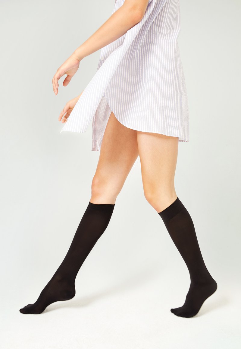 Calze nere fino al ginocchio realizzate in un materiale liscio e elastico. Il design è elegante con un colore uniforme e una vestibilità comoda nella parte superiore.
