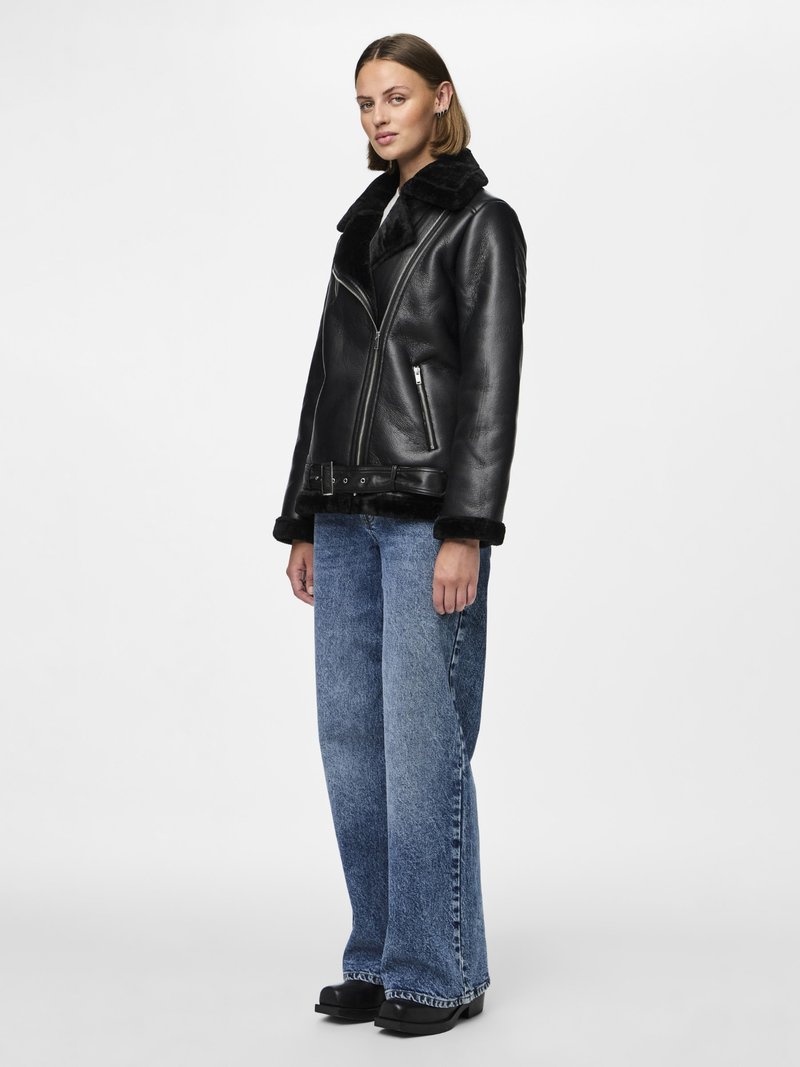 Black leather jacket with a shearling collar, asymmetrical zipper, and side pockets, paired with light blue wide-leg jeans and black boots.