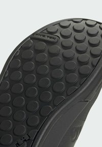 Mustat kumipohjat, joissa on pyöreä kulutuspinta, teksturoitu pinta ja bränditieto reunan varrella. Kestävä ja joustava muotoilu.